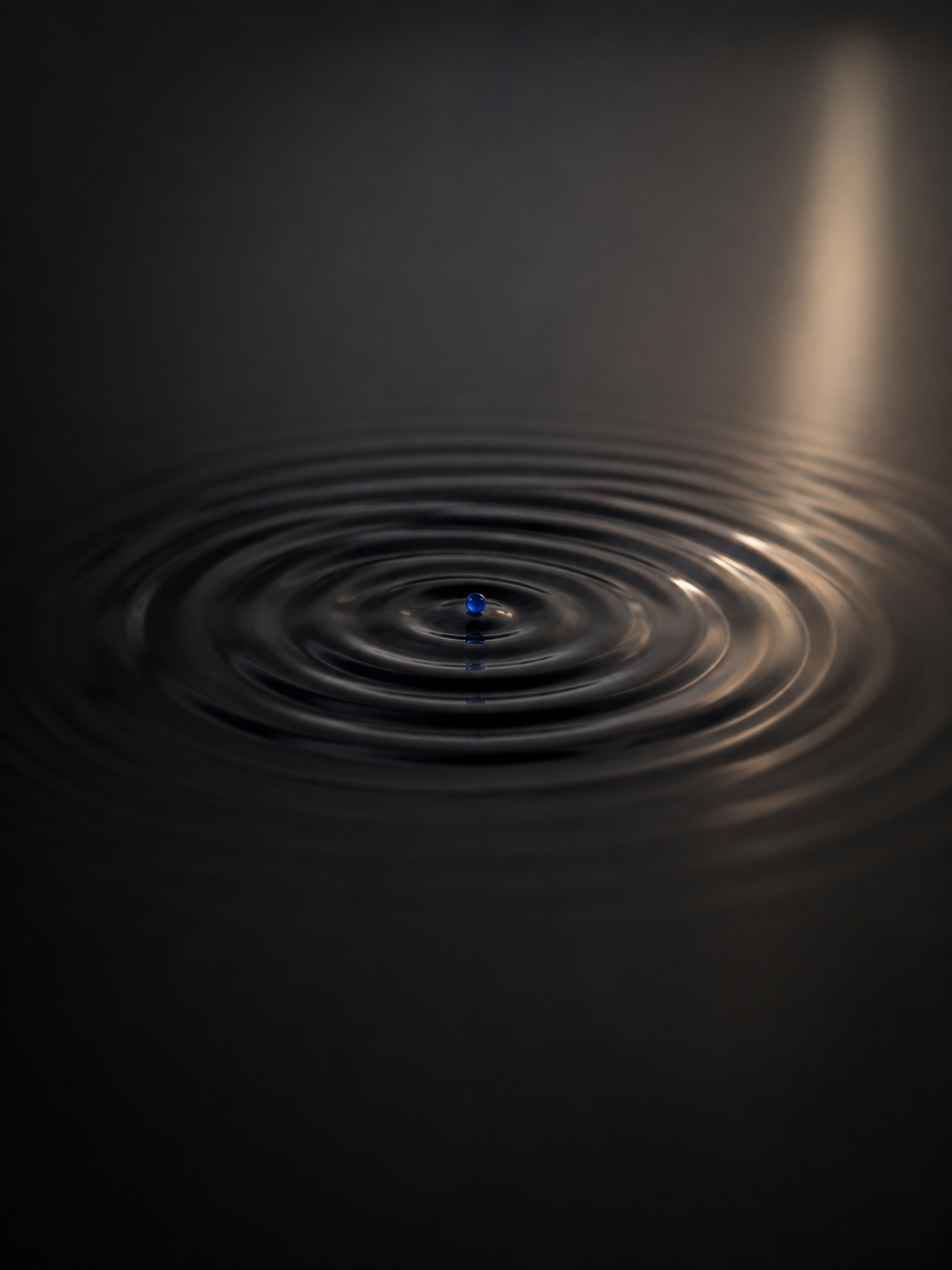 A cobalt point creating ripples across a dark surface